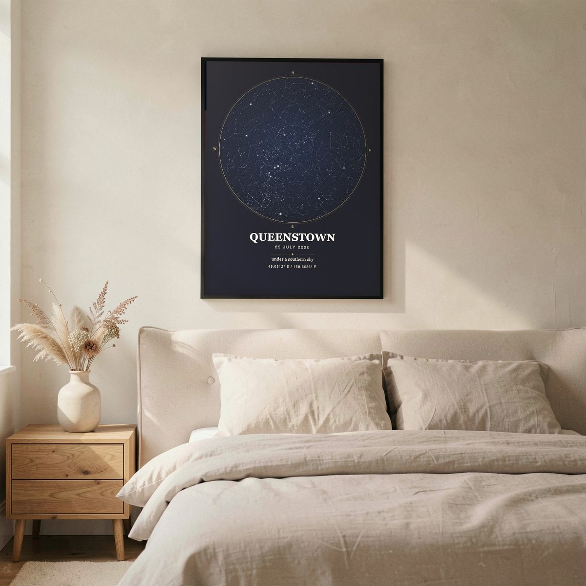 Mockup: a navy Skynolie star map of Queenstown in a black frame above a linen bed